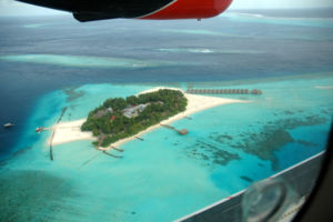 L'isola di Moofushi, ripresa da un idrovolante, ospita un tipico resort turistico maldiviano. Si notino: le barriere coralline che circondano l'isola (appaiono come rocce sottomarine nella laguna turchese); la laguna turchese racchiusa dalle barriere; i muretti artificiali costruiti per preservare la spiaggia dall'erosione stagionale; due pontili d'attracco posti in punti dove l'acqua  pi profonda (si osservi, di fronte al pontile in basso a destra, la spaccata nei coralli operata per permettere alle barche di raggiungere il pontile); a destra dell'isola, le palafitte (comunemente definite overwater) costruite nella laguna; una pass oceanica chiaramente identificabile oltre l'isola come un canale blu; la barriera dell'atollo, visibile nell'estremo angolo in alto a destra (al di l  l'Oceano Indiano aperto).